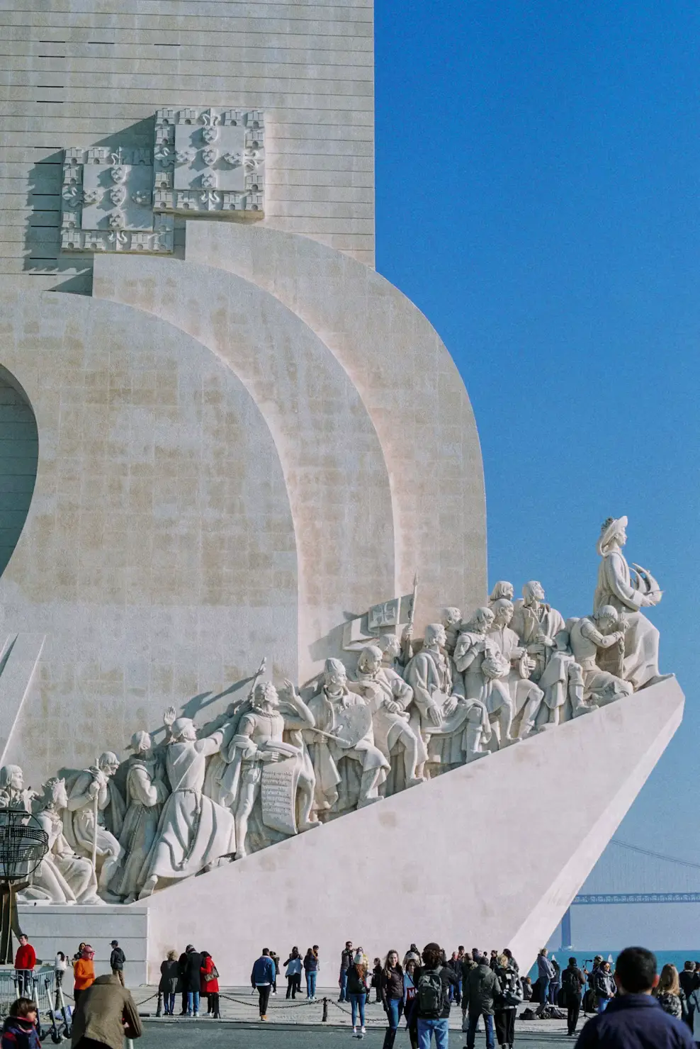 The Monument to the Discoveries with carved historical figures, visitors below, and a clear blue sky.