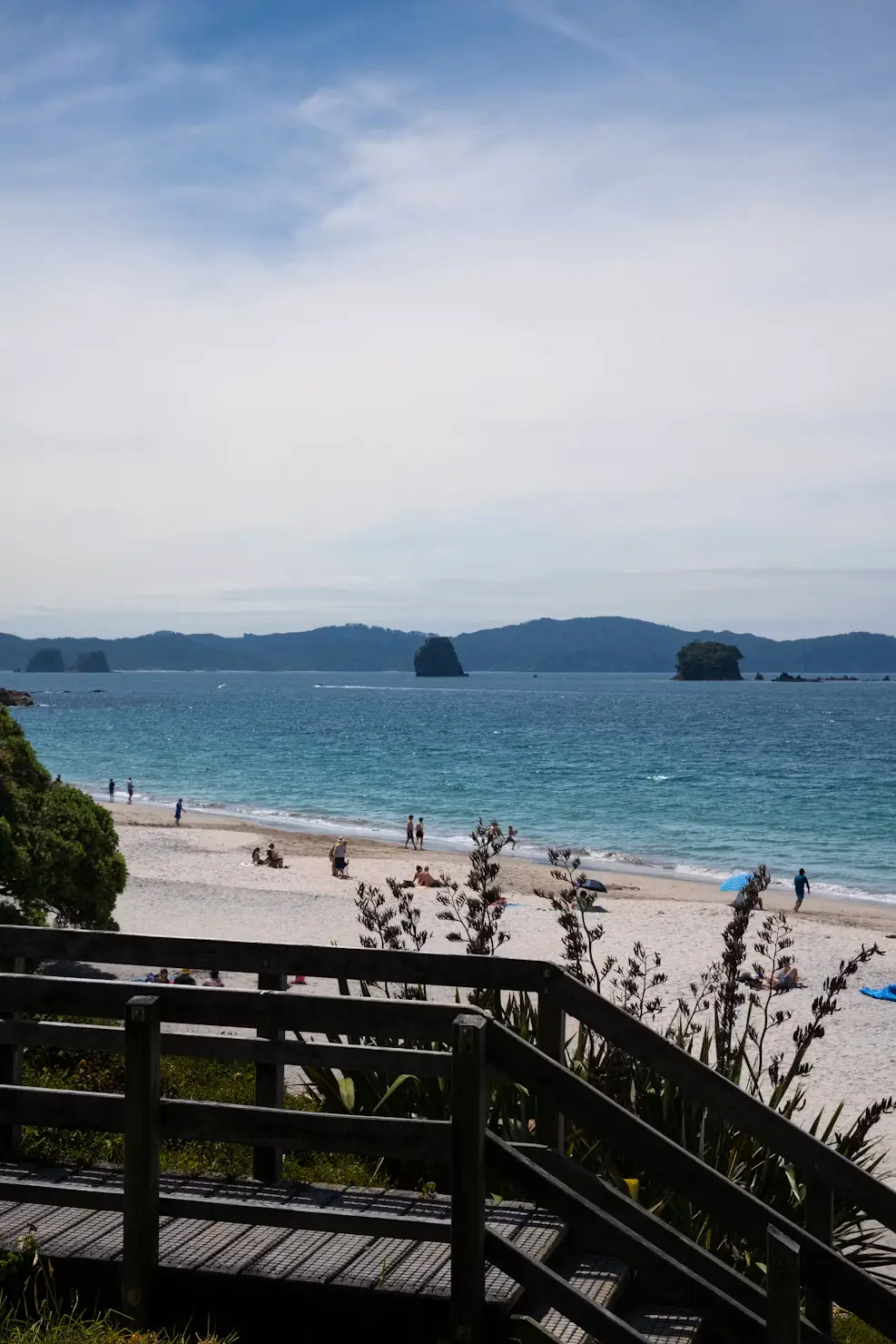 Wooden boardwalk overlooking a white-sand beach with blue water and distant islands.