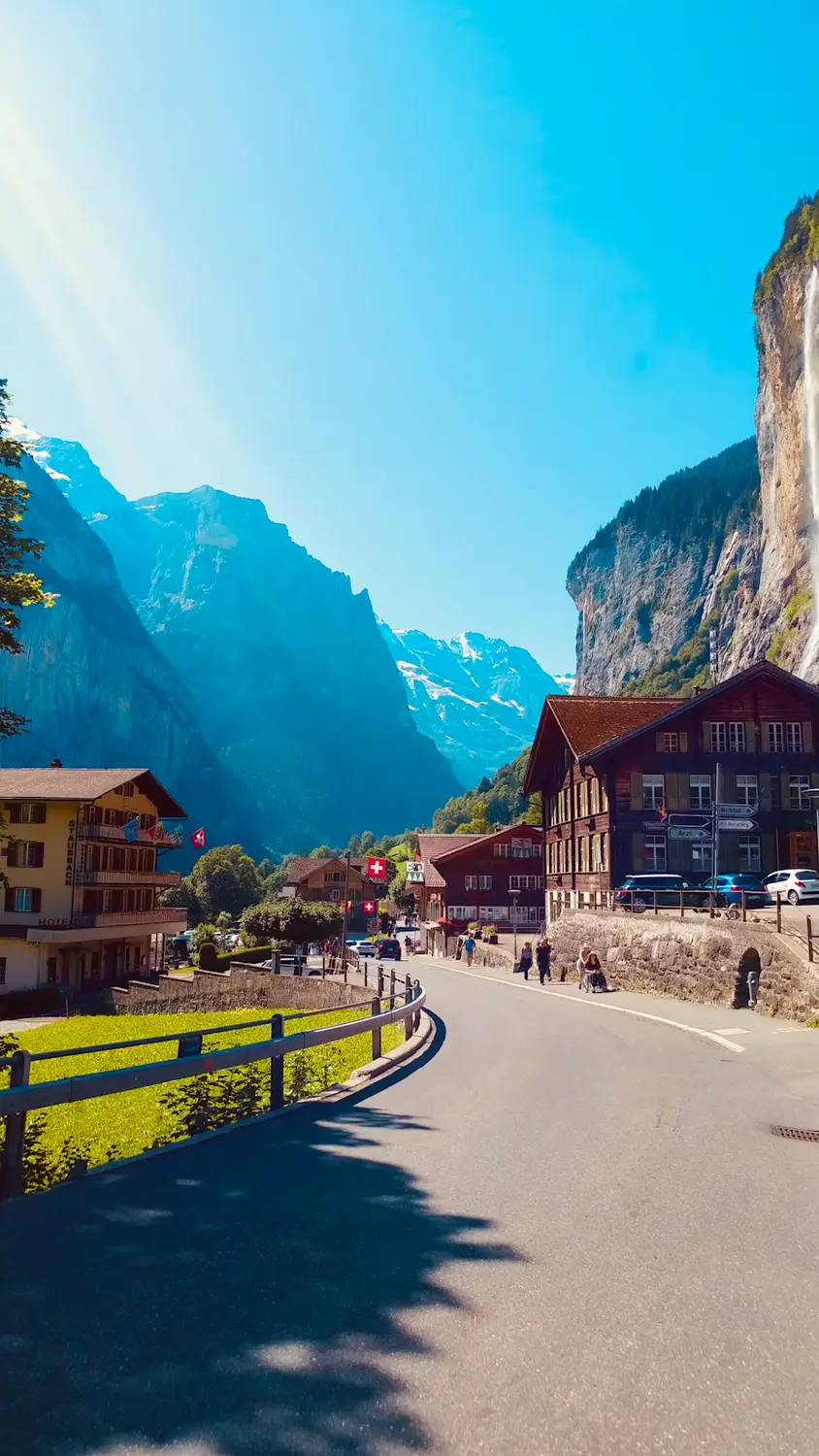 Sunlit village street lined with traditional chalets between steep mountain cliffs, Switzerland