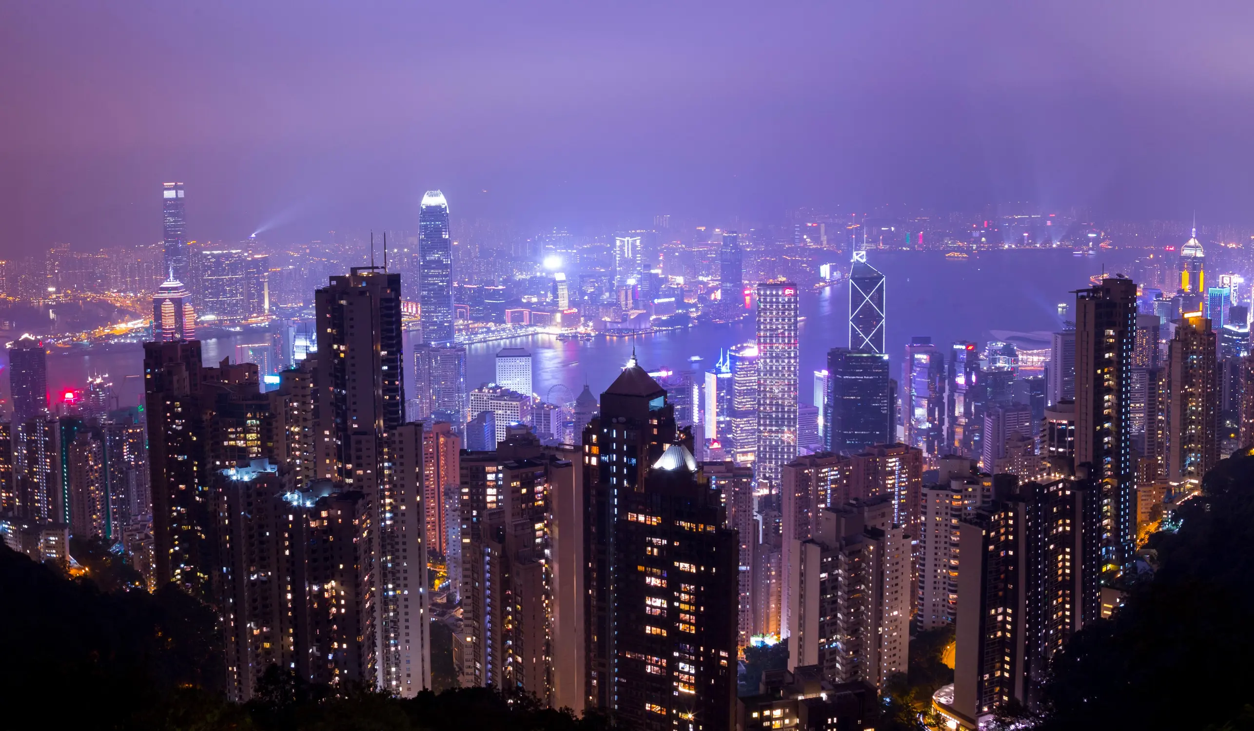 Illuminated Hong Kong skyline at night viewed from Victoria Peak, with glowing skyscrapers and a purple sky in Hong Kong.