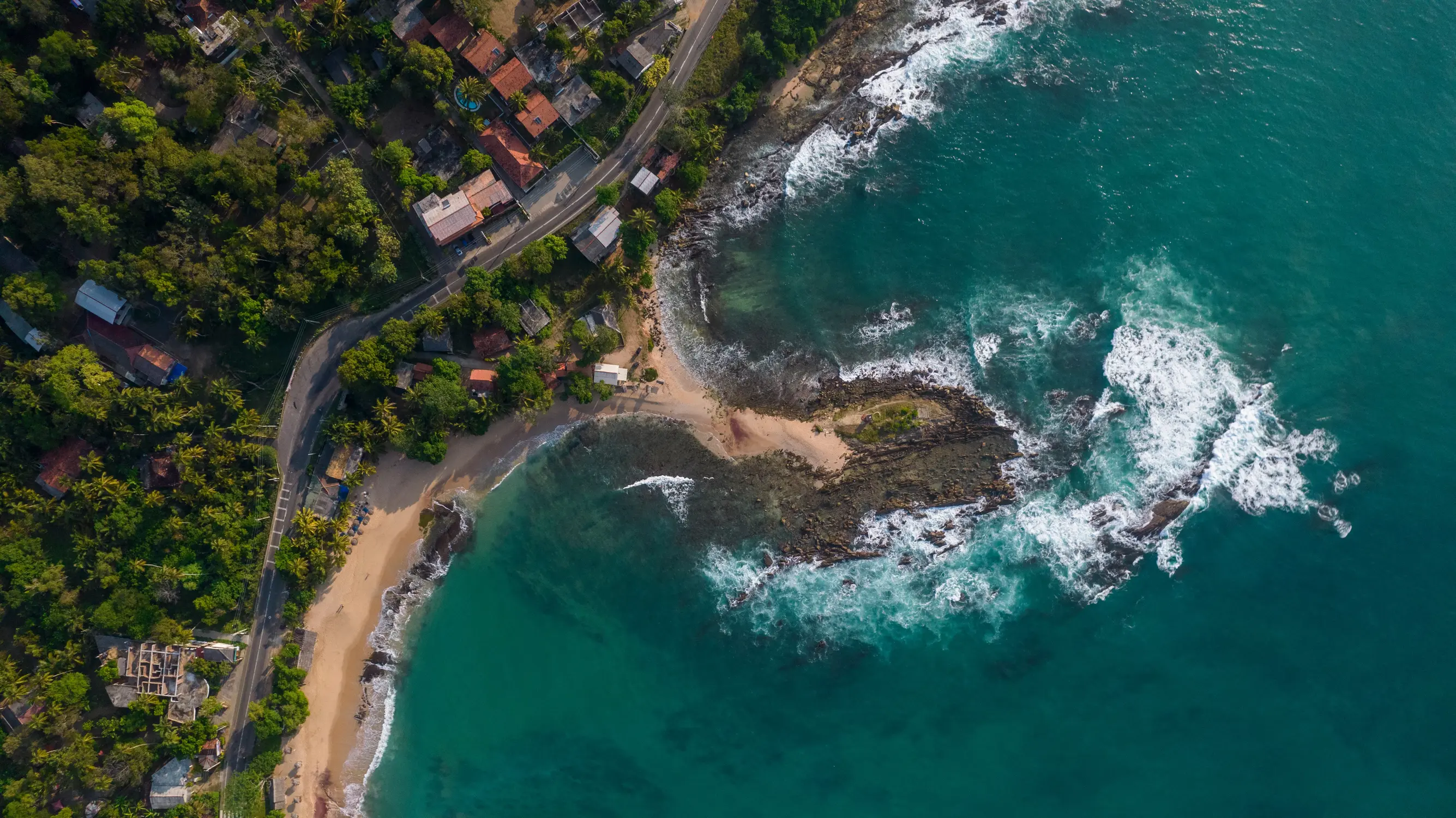 Aerial view of a rugged coastline with turquoise waters, sandy coves, and lush greenery in Sri Lanka.