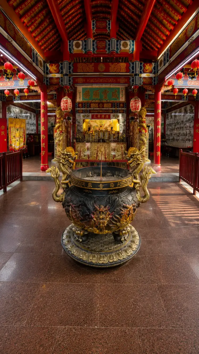 Interior of Brunei Chinese temple with large bronze dragon incense burner, red lanterns and gilded altar shrine
