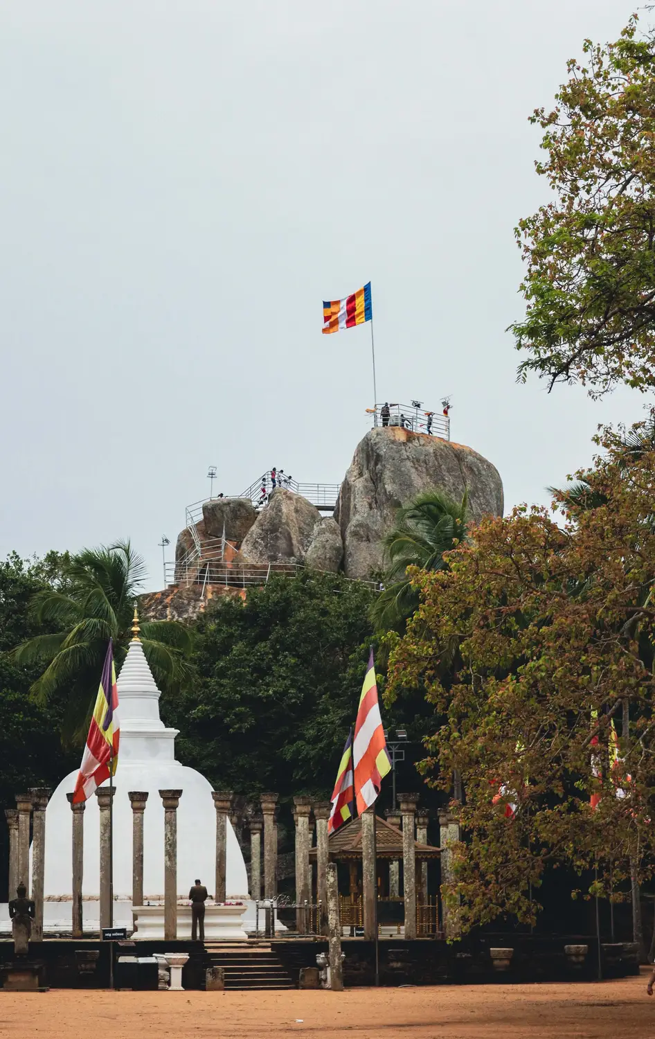 White Buddhist stupas with a Sri Lankan Buddhist flag and a rock outcrop in the background in Sri Lanka.