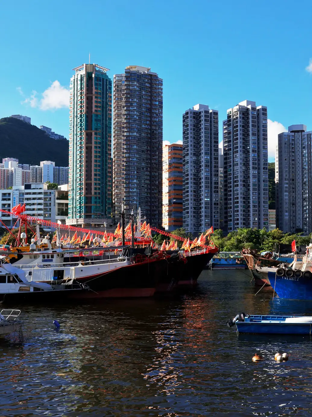 Colorful fishing boats moored in a harbour with modern high-rise apartment towers in the background in Hong Kong.