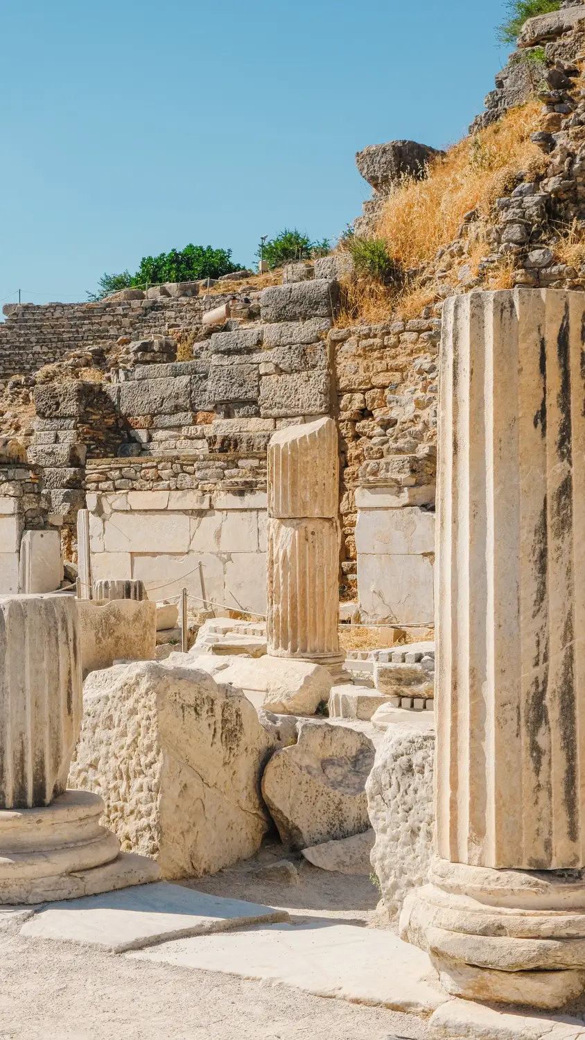 Ancient stone ruins with a fallen column lying among scattered fragments of an archaeological site.