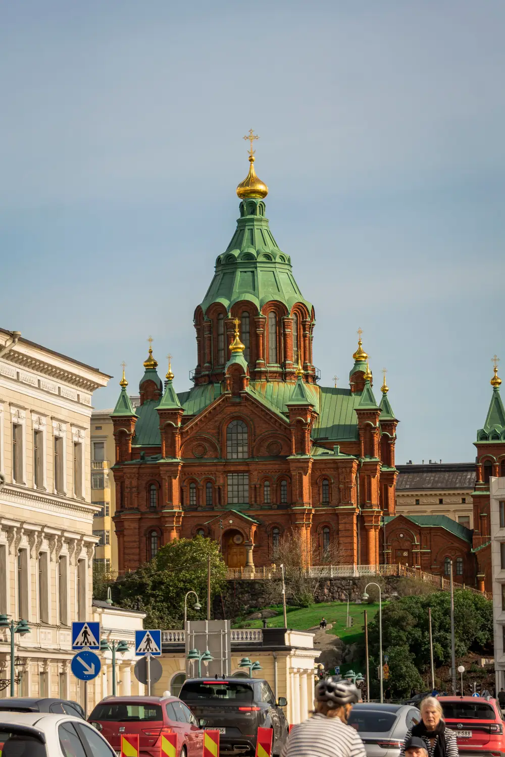 Uspenski Cathedral, a red-brick Orthodox church with green and gold domes, overlooking a busy Helsinki street.
