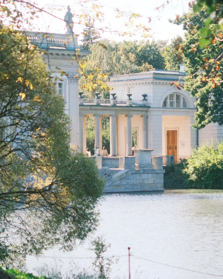 Elegant historic white building beside a calm waterfront, surrounded by trees.