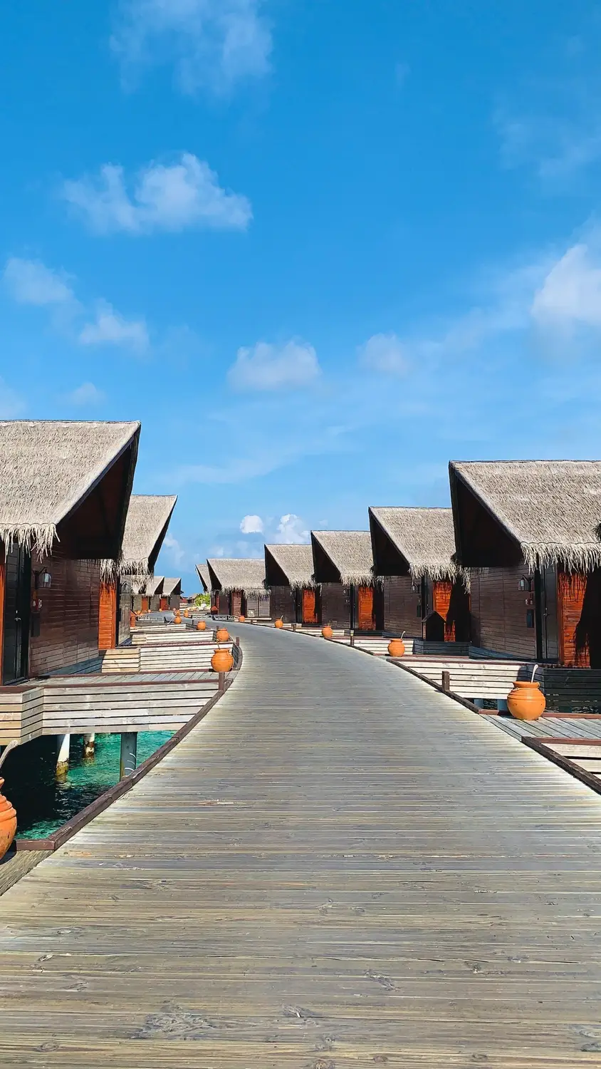 Wooden boardwalk path lined with thatched roof overwater bungalows and clay pot decorations over turquoise lagoon at Maldives luxury resort