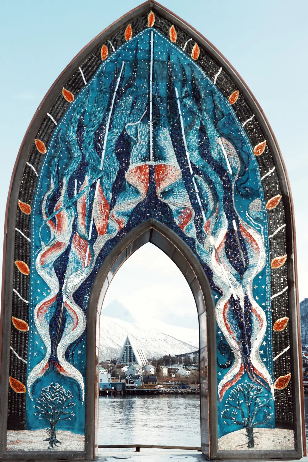 An ornate arched monument decorated with a blue mosaic, framing a view of water and mountains through its opening.