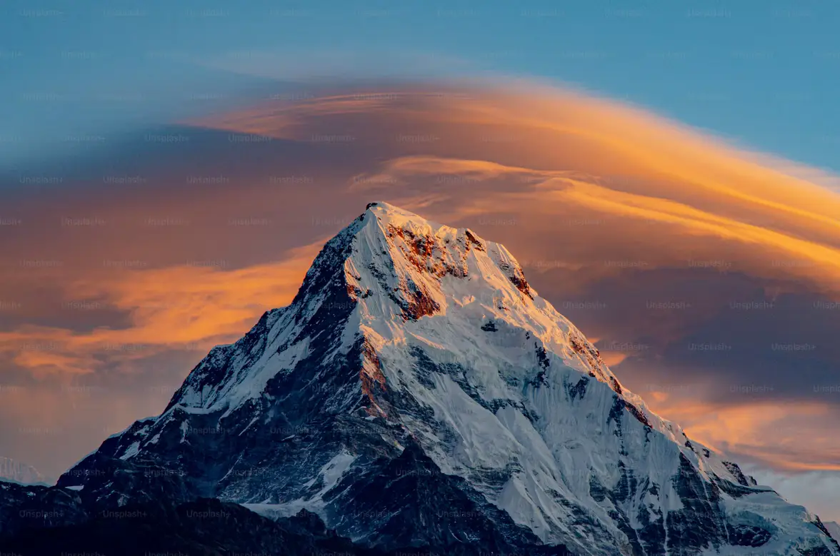 Snow-capped Annapurna peak glowing at sunrise with orange clouds, Nepal Himalayas