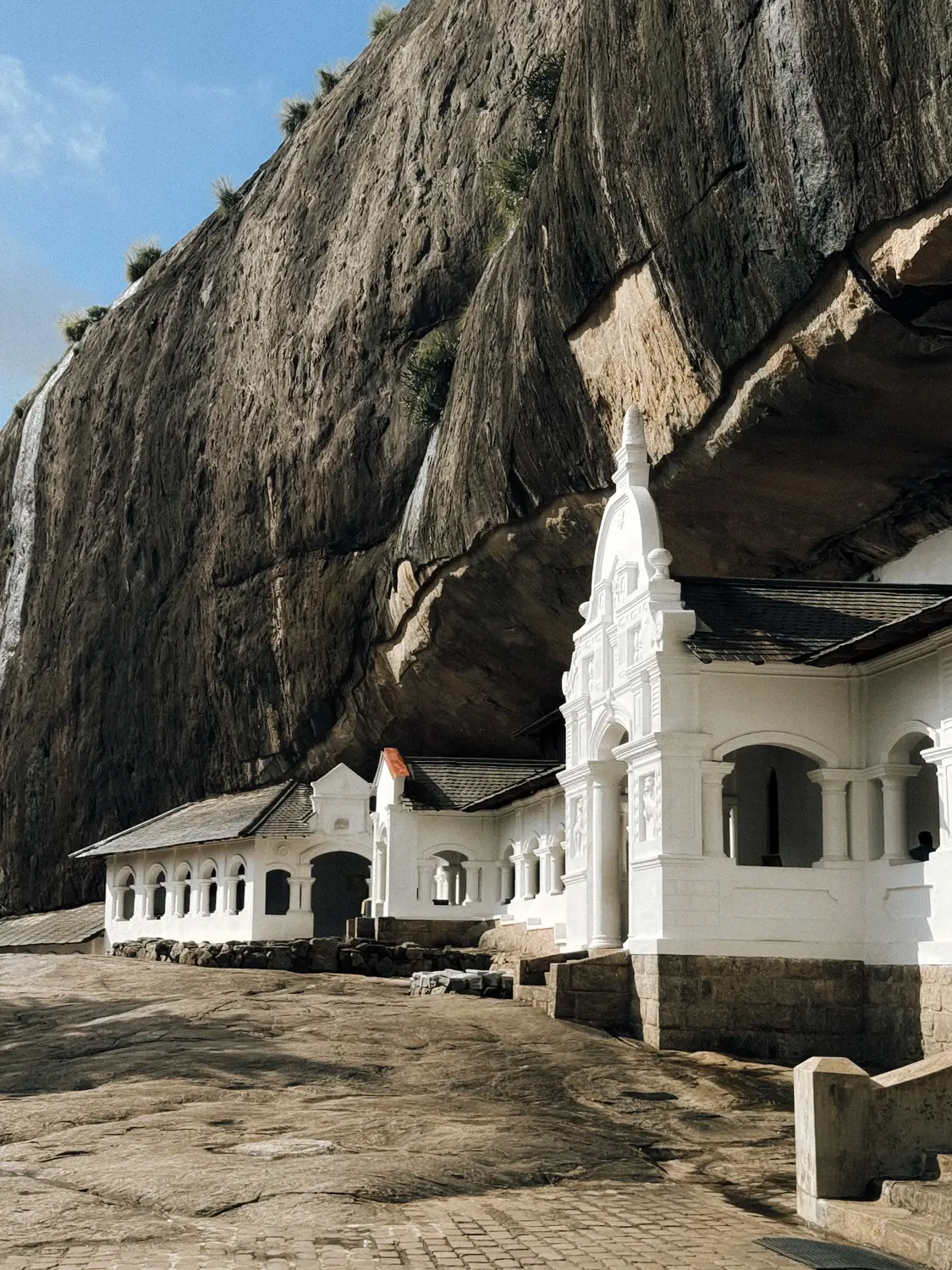 White cave temple built beneath an overhanging rock face at Dambulla, Sri Lanka.