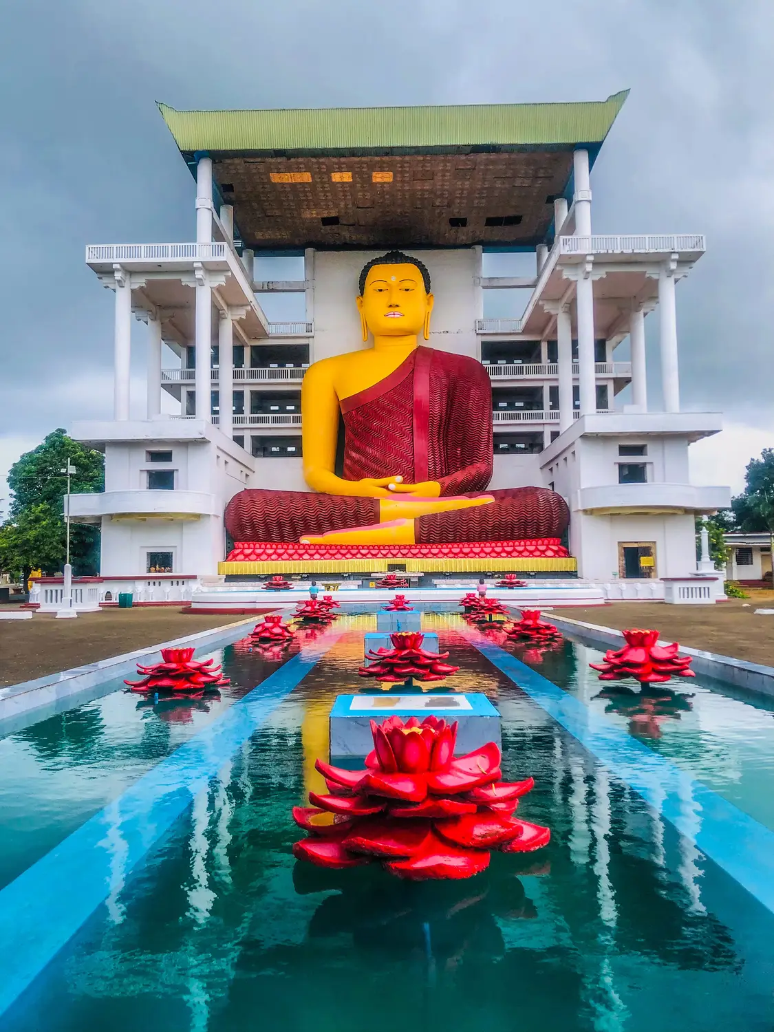 Large golden seated Buddha statue above a lotus-filled reflecting pool at the Golden Temple in Dambulla, Sri Lanka.