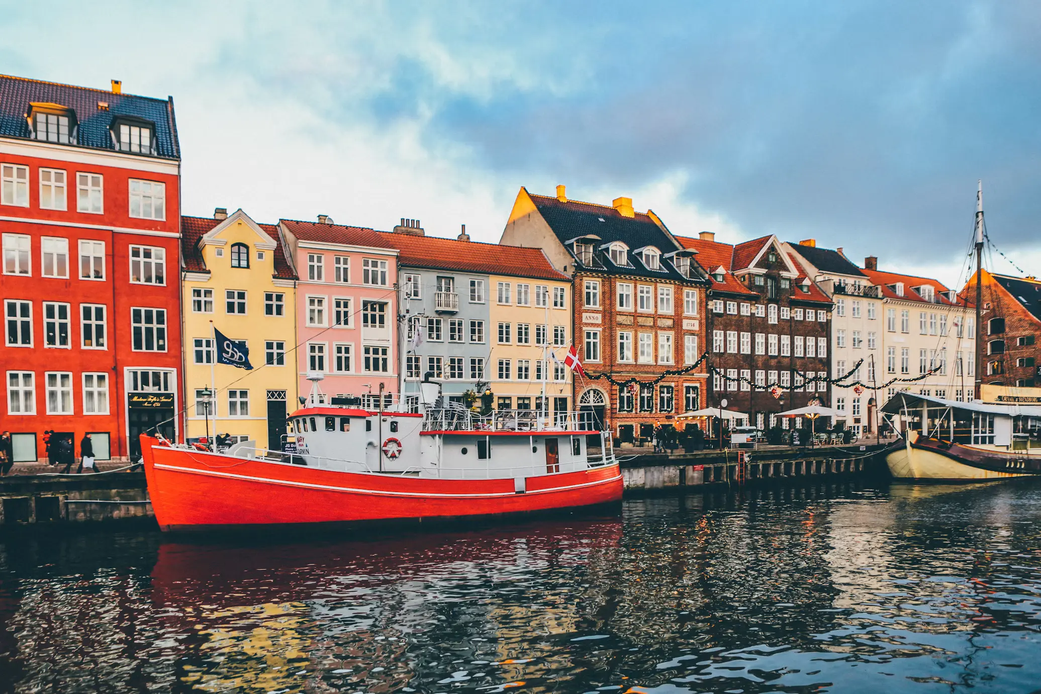 A red fishing boat moored along Nyhavn canal in Copenhagen, Denmark, in front of a row of colorful gabled townhouses