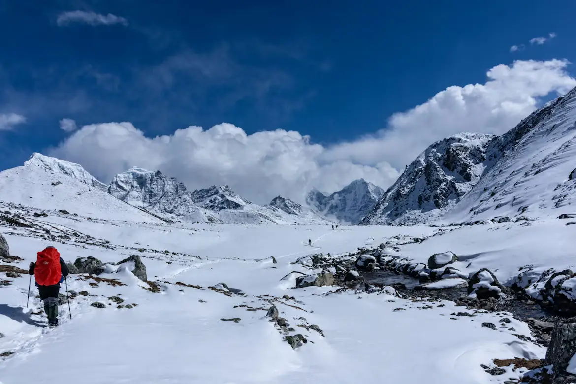 Trekker in a red jacket crossing a snow-covered valley surrounded by Himalayan peaks, Nepal