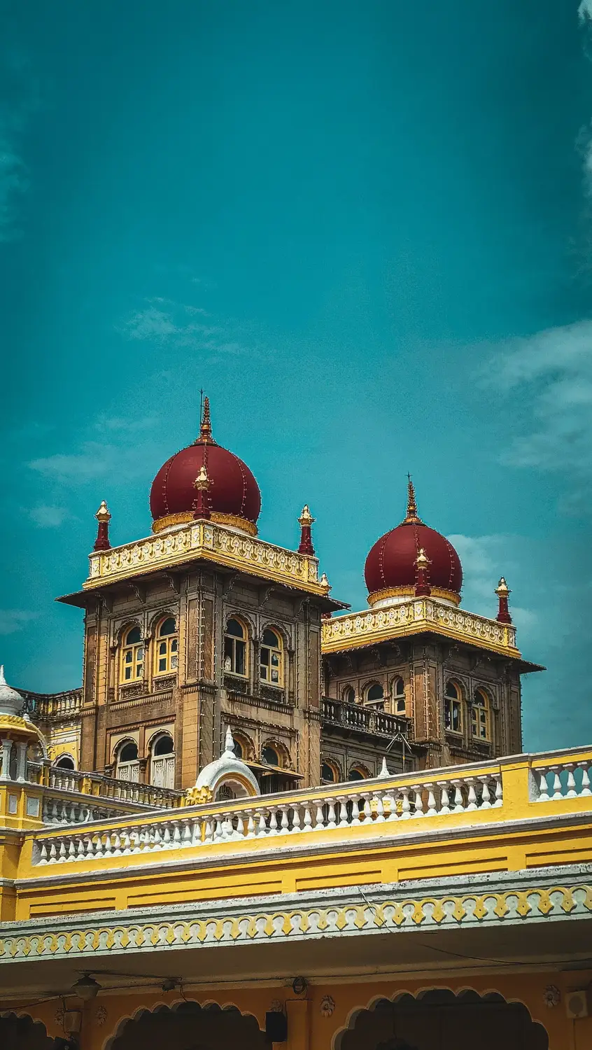 Mysore Palace ornate Indo-Saracenic towers with deep red domes and gold detailing against teal sky, Karnataka, India