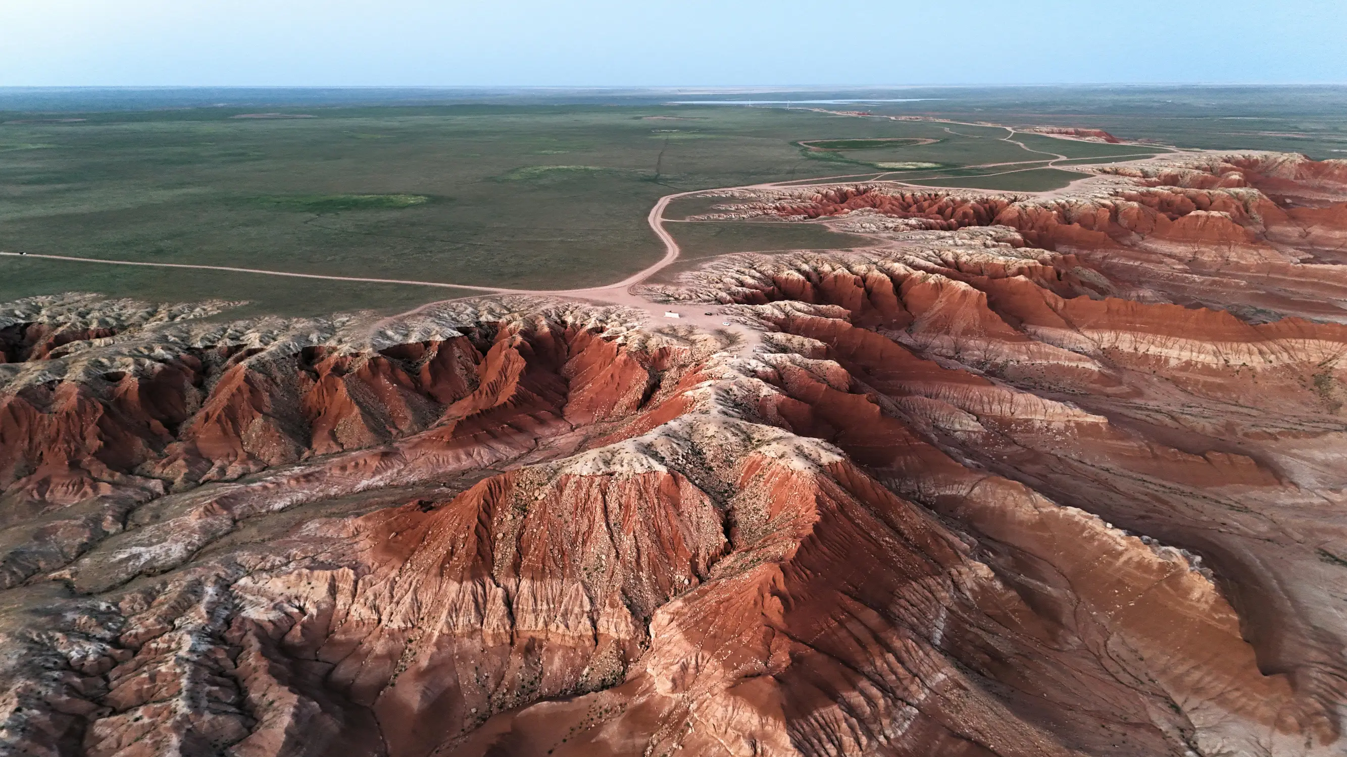 Eroded red sandstone badlands in the Gobi Desert, Mongolia, with vast green steppe plains and a dirt road stretching to the horizon