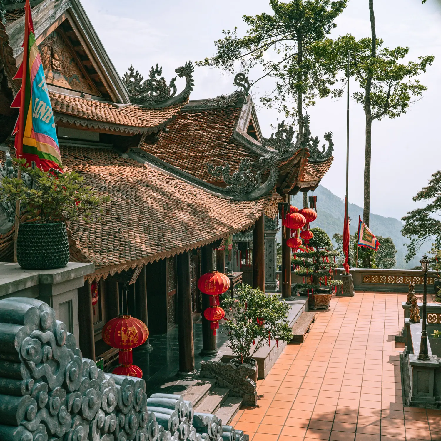Ancient temple with ornate tiled roofs, red lanterns, and a peaceful courtyard surrounded by trees and distant mountains