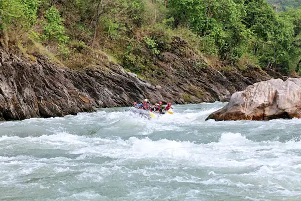 Whitewater raft navigating rapids on a river lined with green forested hills, Nepal