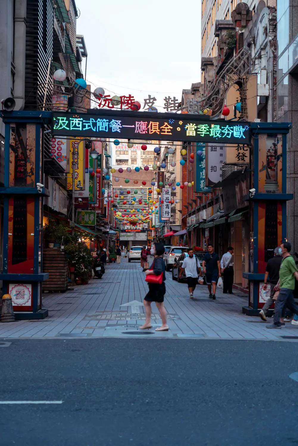 People walking through the LED-lit entrance gateway to Yuanling shoe street in Taipei, decorated with colorful hanging lanterns