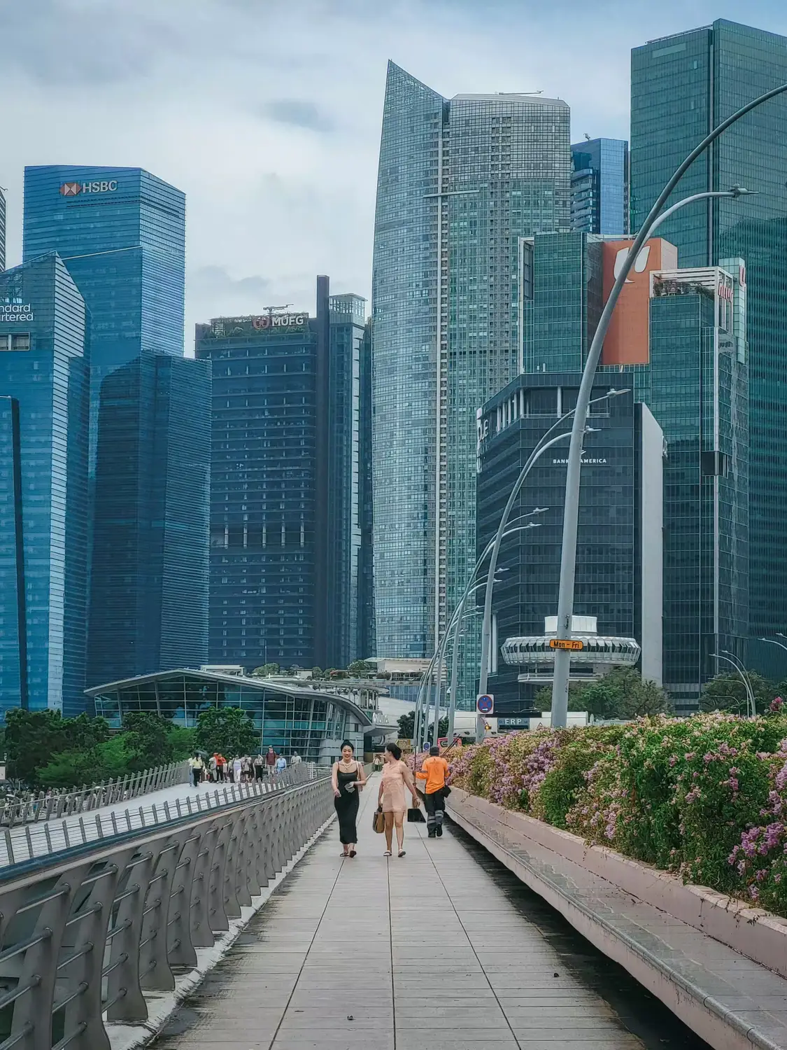 Pedestrians walking along elevated bridge walkway with Singapore Marina Bay CBD skyscrapers in background