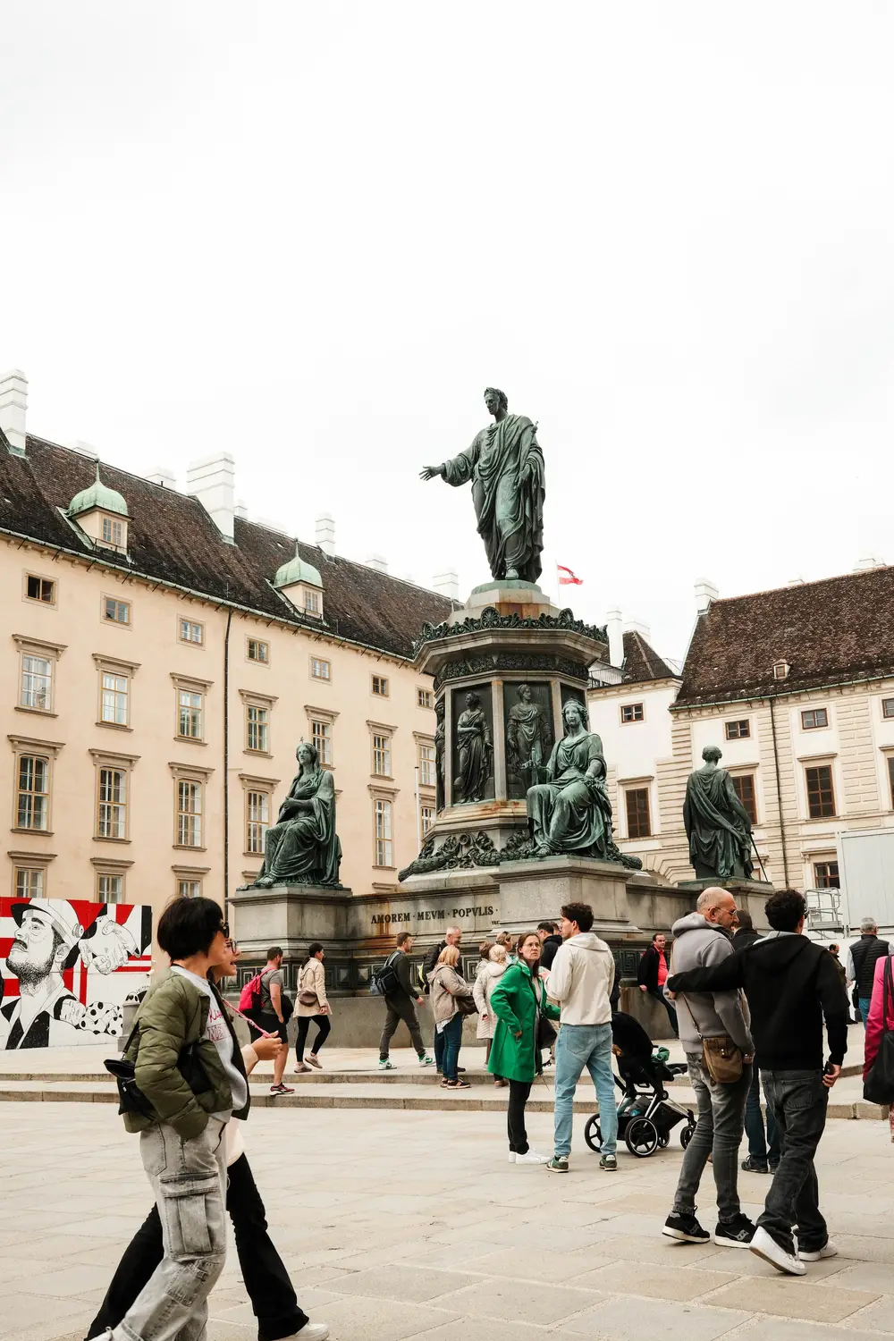 A historic plaza with a bronze equestrian statue, ornate buildings, and people walking across the square.