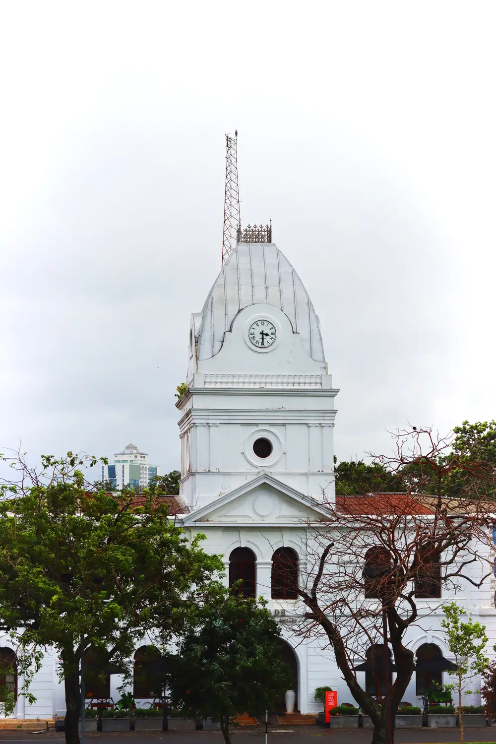 White colonial-style church with a tall clock tower framed by trees in Sri Lanka.