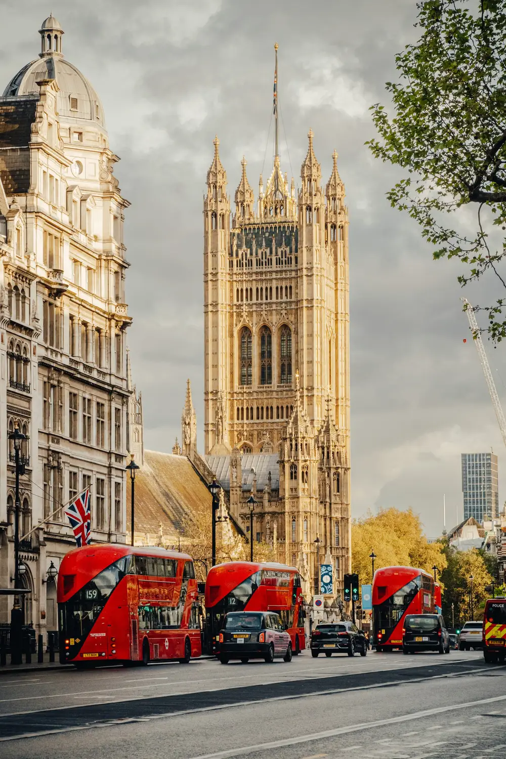 Sunlit gothic tower of the Houses of Parliament with red double-decker buses passing on the street below.