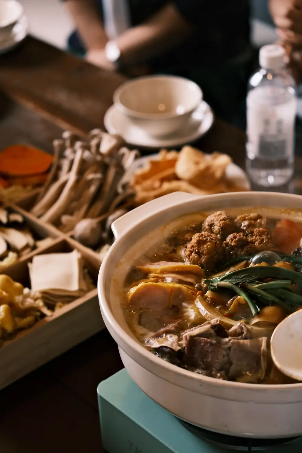 Traditional Chinese hot pot with meatballs, vegetables, and mushrooms served in ceramic bowl with ingredients tray