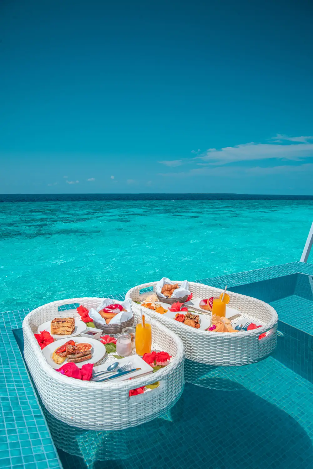 Luxury floating breakfast basket with tropical fruits and drinks on overwater villa deck overlooking turquoise ocean lagoon in Maldives