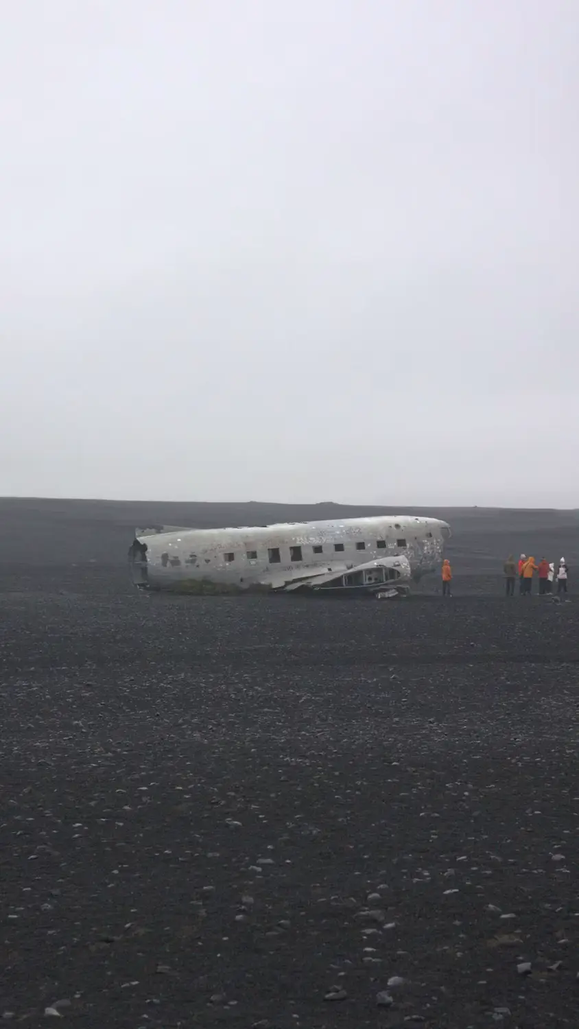 Abandoned plane wreckage resting on a black sand beach under an overcast sky, Iceland.