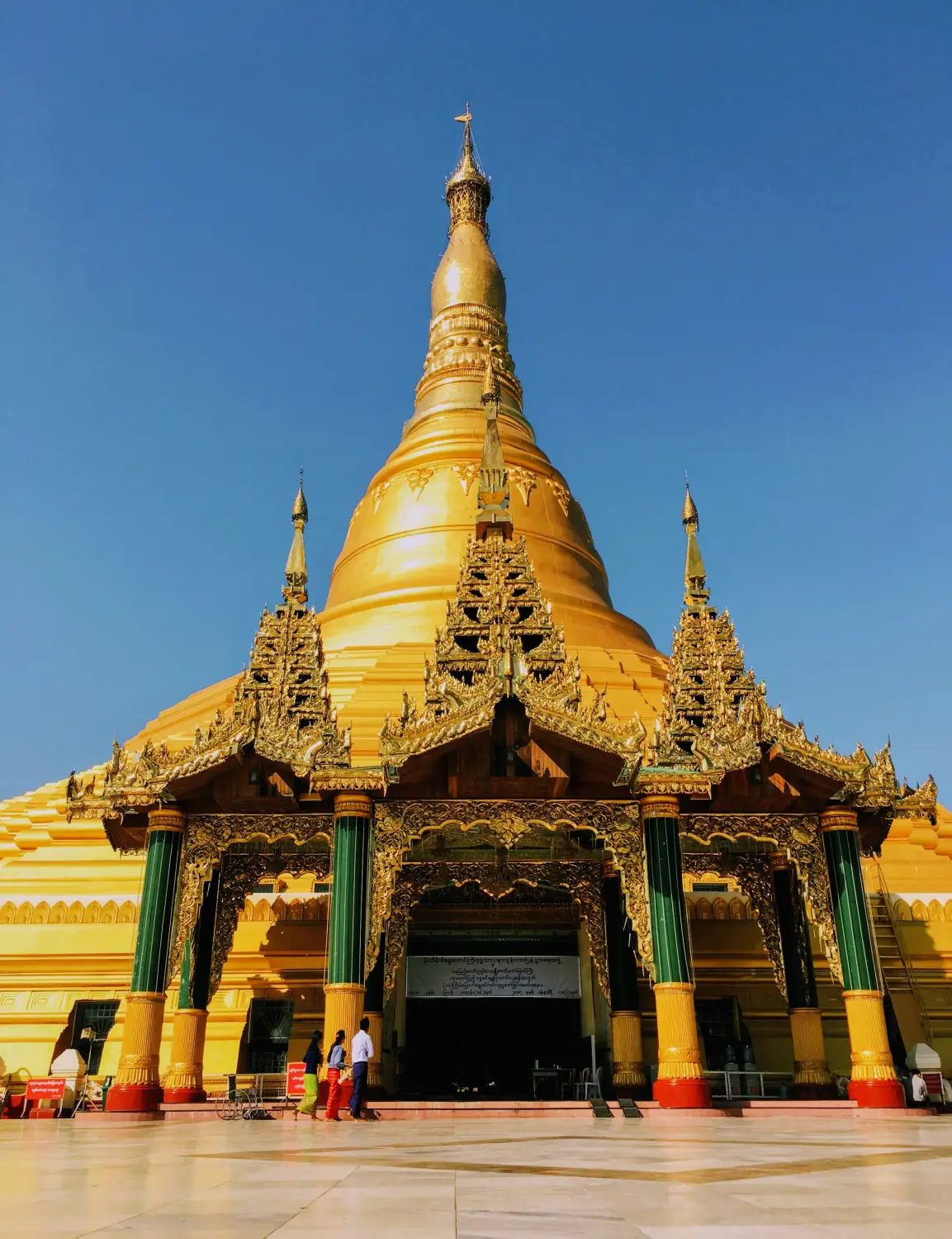 Golden Shwemawdaw Pagoda with intricate tiered spire and ornate entrance gate against clear blue sky, Bago Myanmar