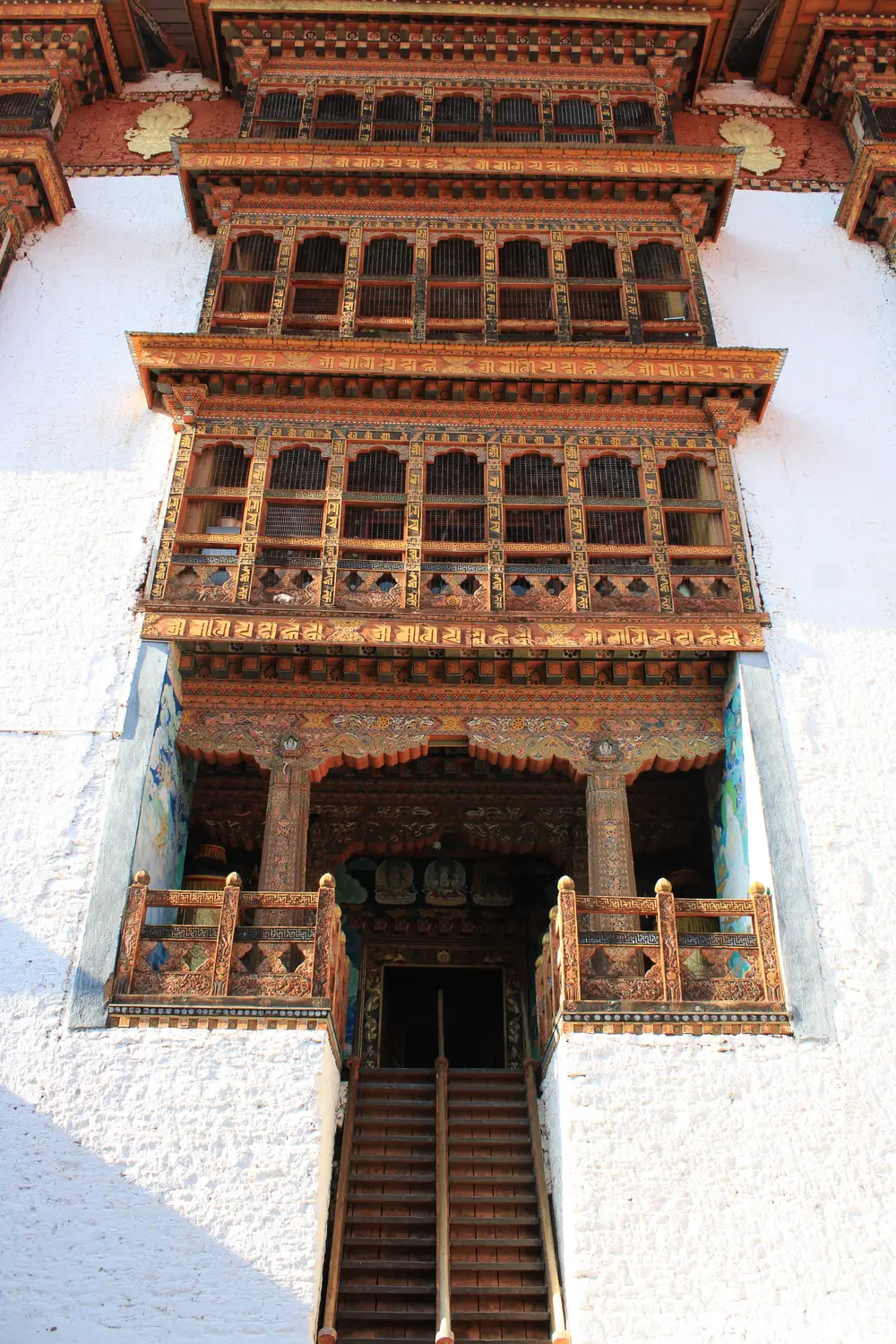 Ornate carved wooden facade and windows of a traditional Bhutanese dzong with a central staircase in Bhutan.