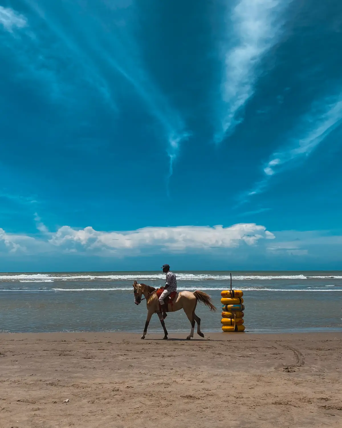 Man riding a horse along Cox's Bazar sea beach under dramatic blue sky with ocean waves in background, Bangladesh