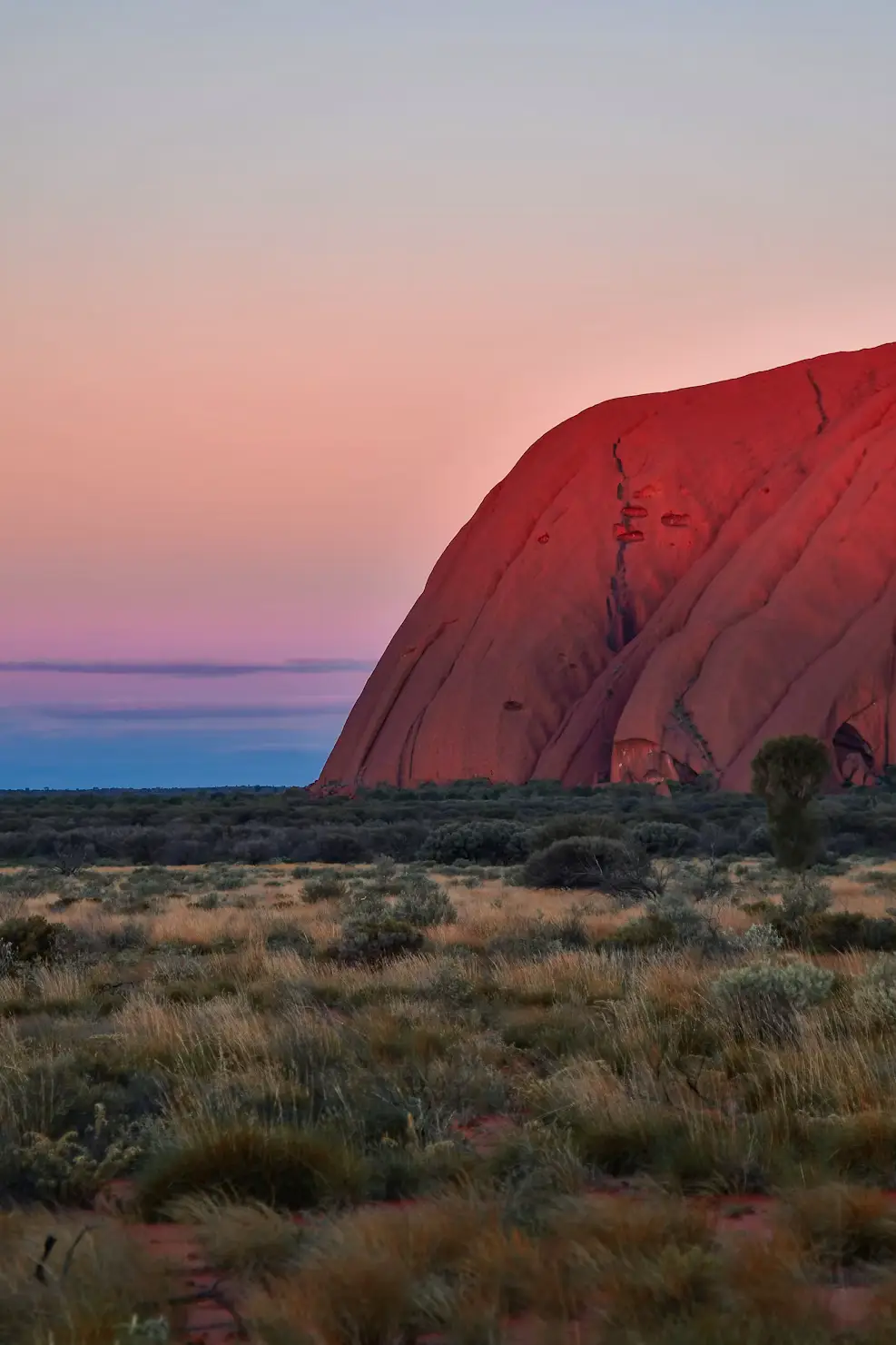 Uluru rock formation glowing red at sunset in the Australian outback