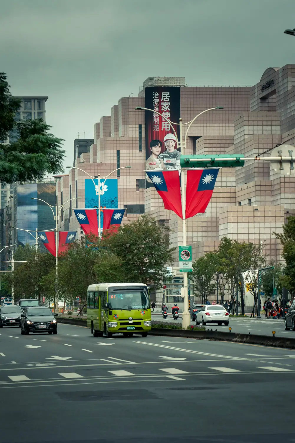 Green city bus on a Taipei boulevard lined with Taiwan flags and a department store in the background