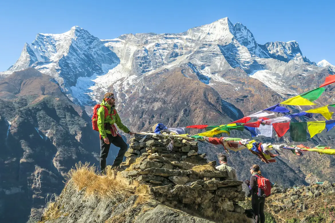 Hiker resting on a rocky ridge beside Buddhist prayer flags overlooking snow-capped Himalayan peaks, Nepal