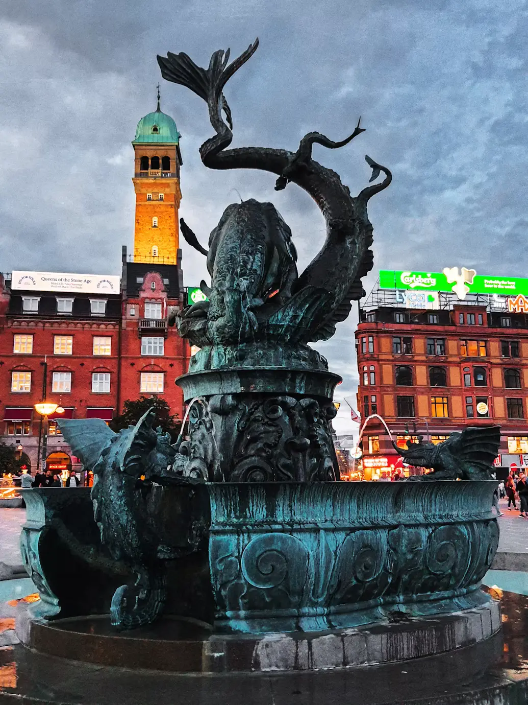 Bronze mermaid statue on a fountain in a Copenhagen square with historic red buildings behind