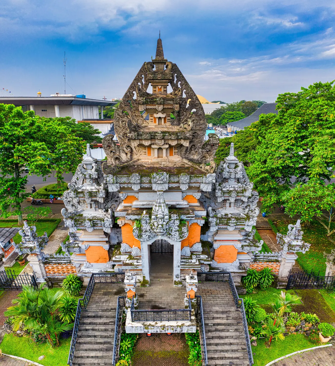 Balinese water temple Pura Ulun Danu Beratan with tiered pagoda towers on the shore of Lake Bratan, surrounded by mist-covered mountains in Bali, Indonesia.do for thisOrnate Balinese stone temple gate with intricate carvings and a tiered tower, flanked by lush green trees and stone staircases under a blue sky in Indonesia.