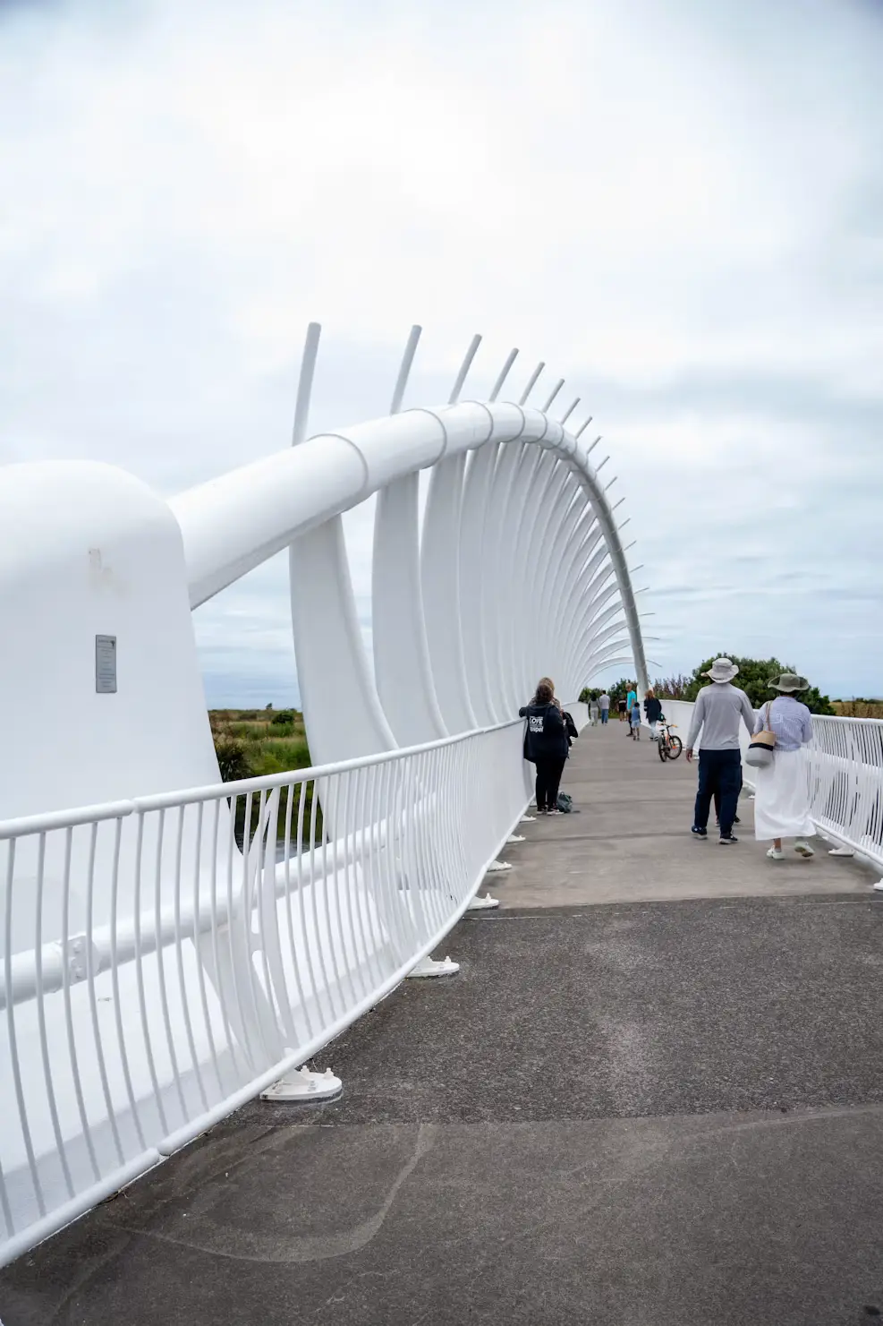 White curved pedestrian bridge with people walking beneath sweeping rib-like arches.