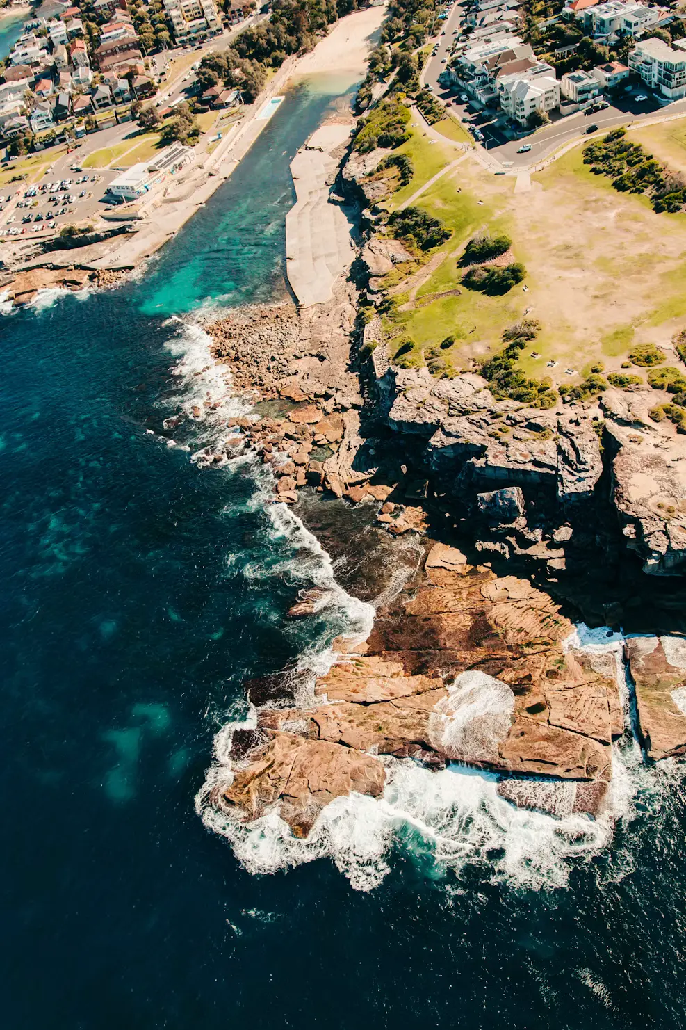 Aerial view of a rocky ocean headland with waves crashing near a coastal town, New South Wales, Australia