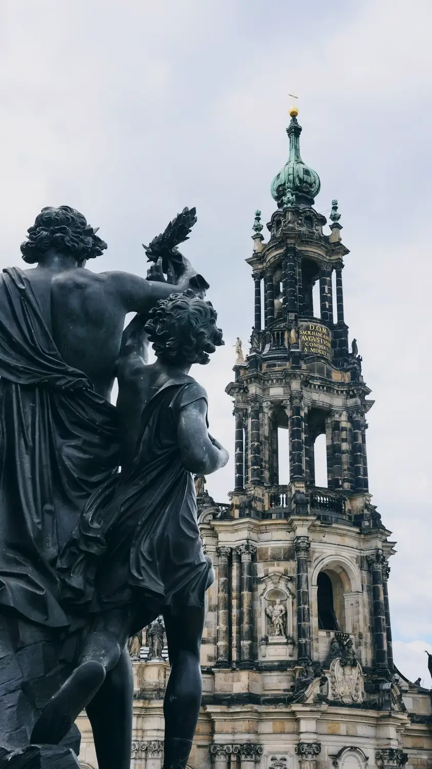 Statue in the foreground with a Baroque church spire rising behind in Dresden