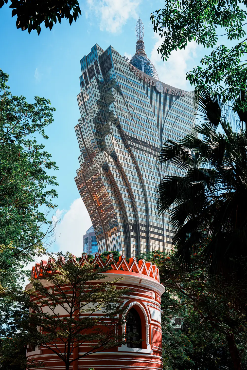 Grand Lisboa tower viewed through trees behind an ornate red pavilion roof