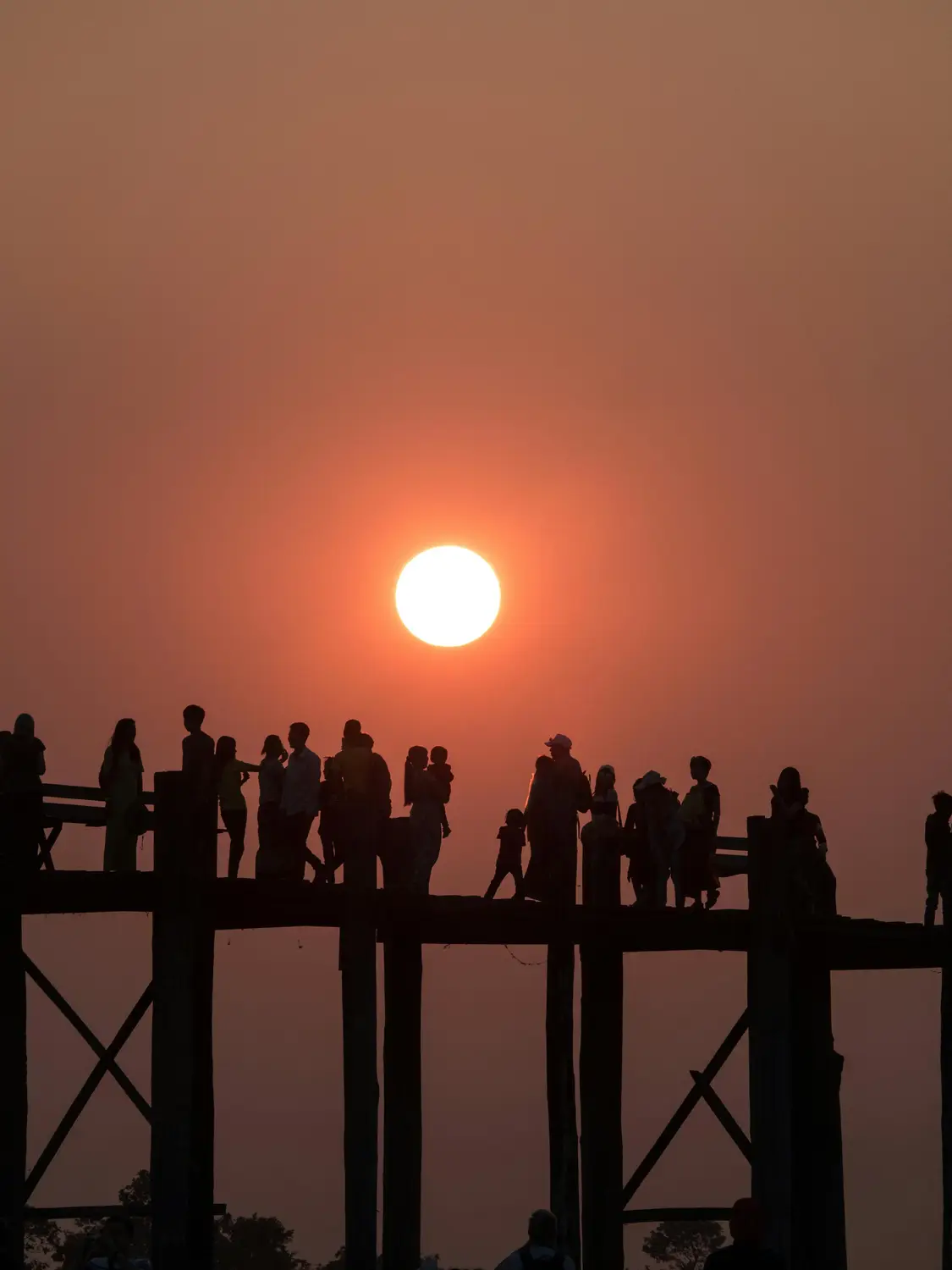 Silhouettes of crowd of people on U Bein teak bridge at dramatic orange sunset over Taungthaman Lake, Mandalay Myanmar