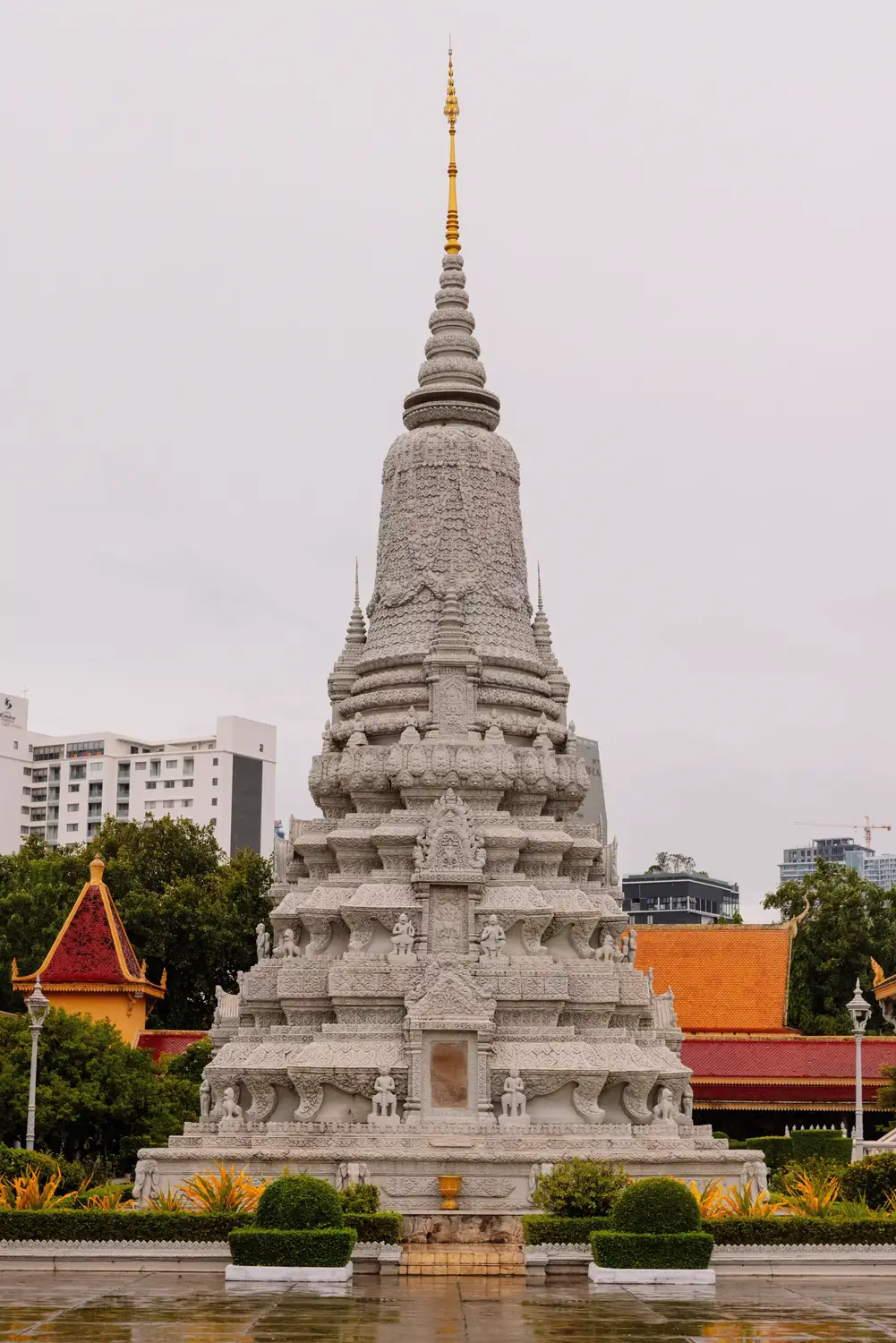 Aerial drone view of ornate golden Cambodian Buddhist temple with tiered orange roof surrounded by green trees and pond, Cambodia