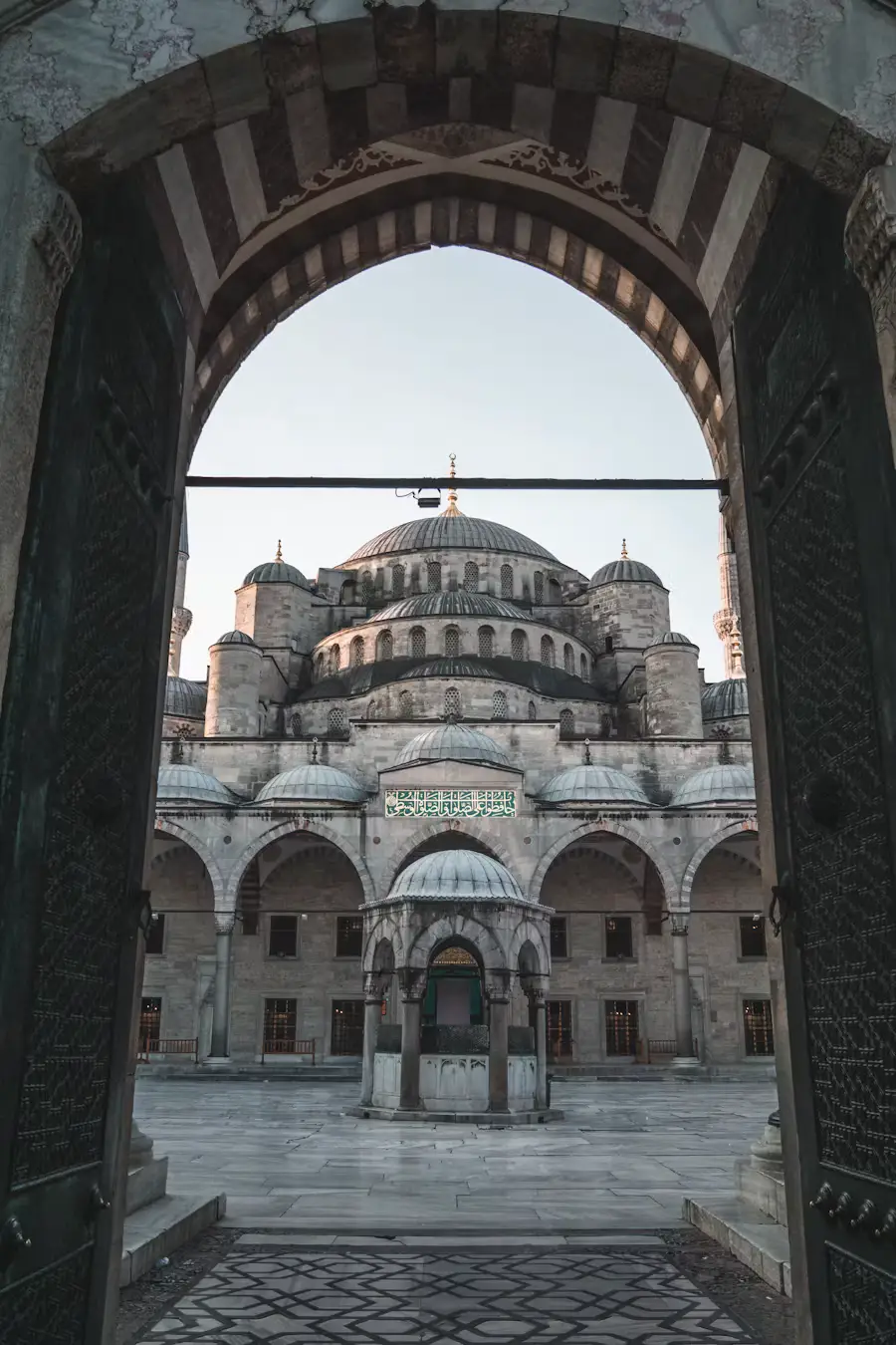 The courtyard and domed structure of the Blue Mosque, framed by a stone archway.