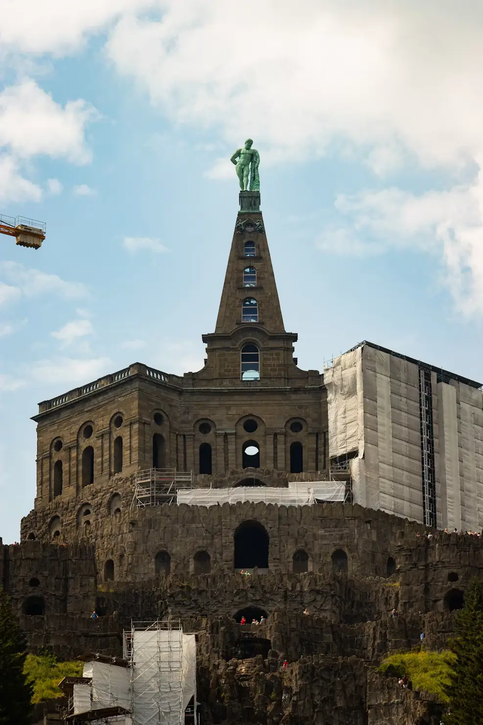 Historic stone fortress tower with statue, viewed from below against a cloudy sky