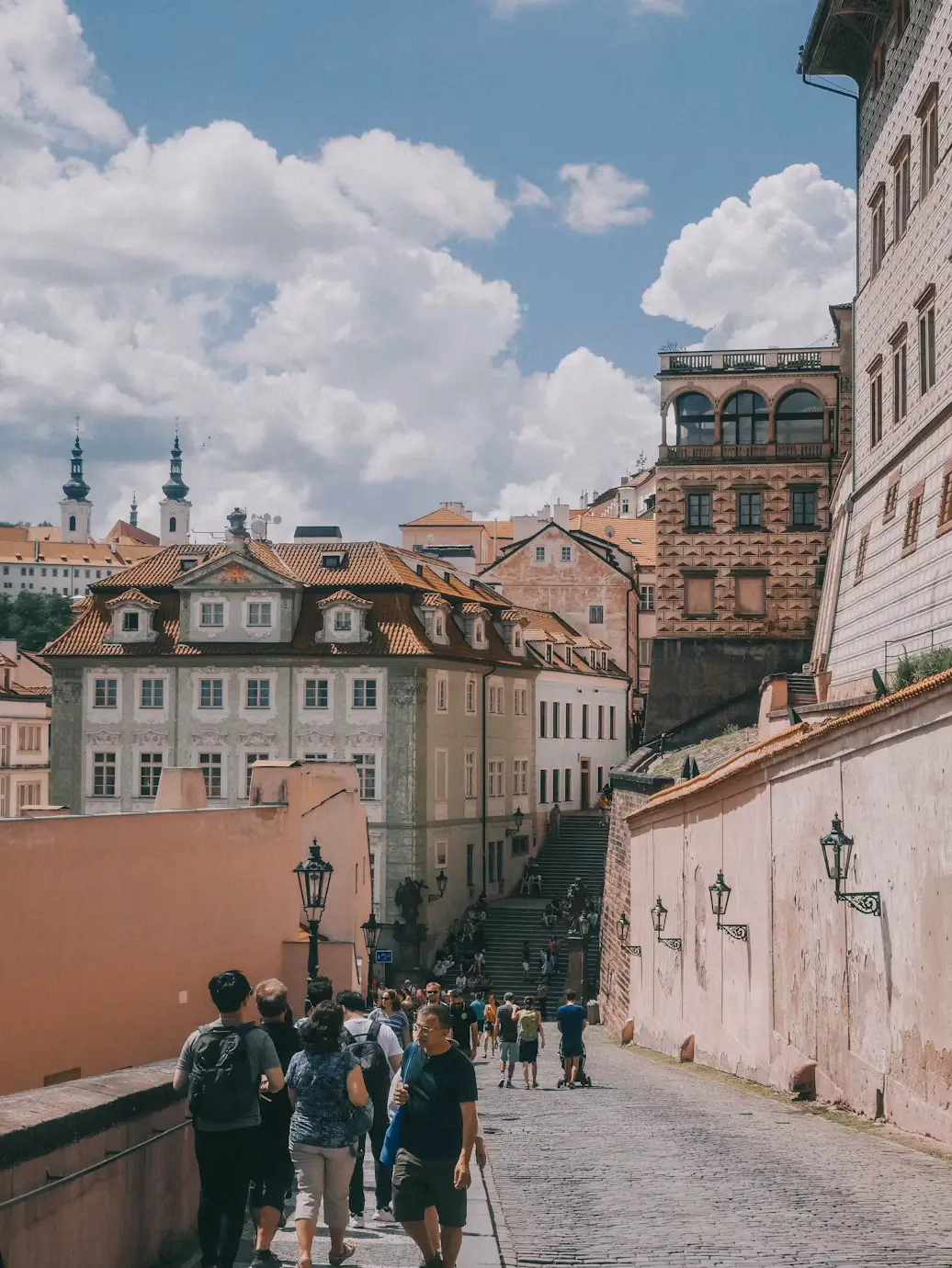 Pedestrians walking along a narrow street lined with pastel buildings in Prague's Malá Strana district
