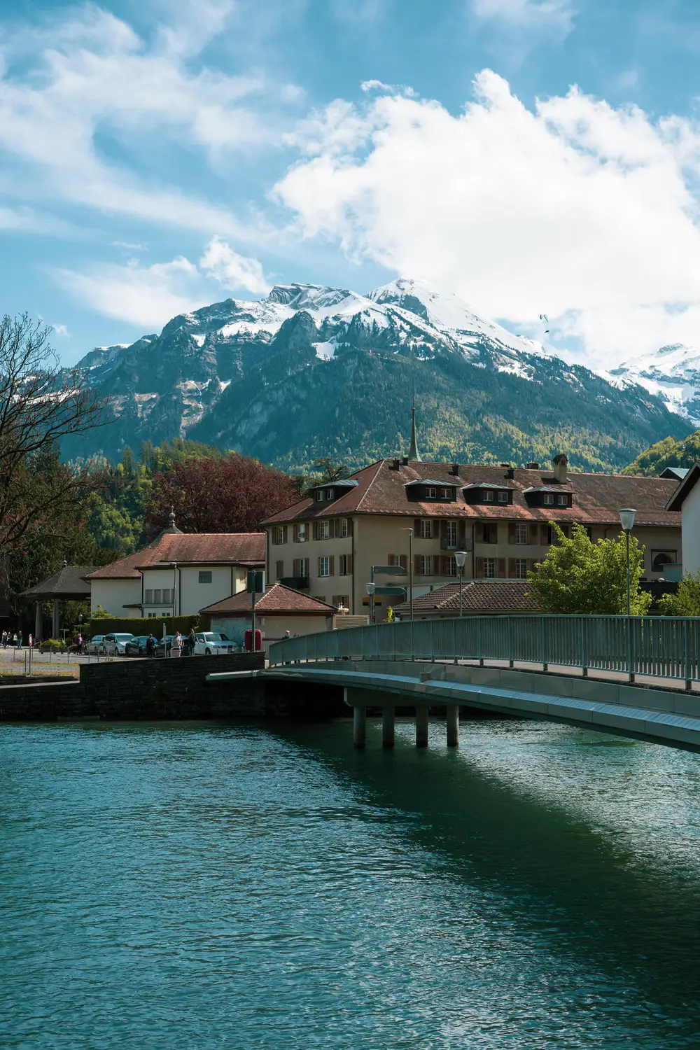 River flowing through town with a footbridge and snow-capped mountains in the background, Switzerland