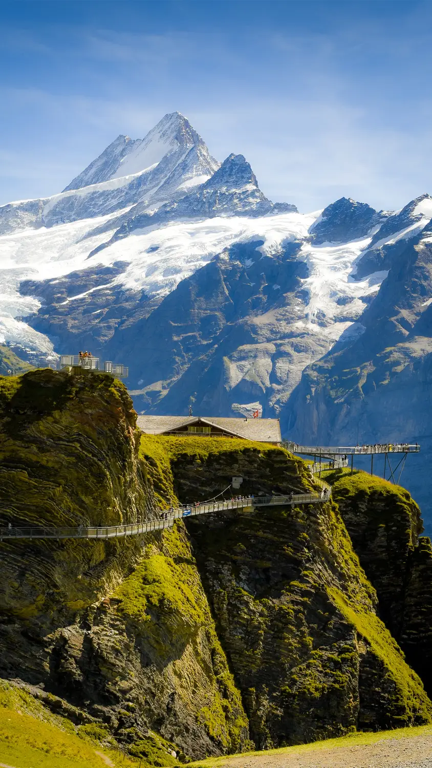 Suspension bridge over a rocky cliff with snow-capped mountain in the background, Switzerland