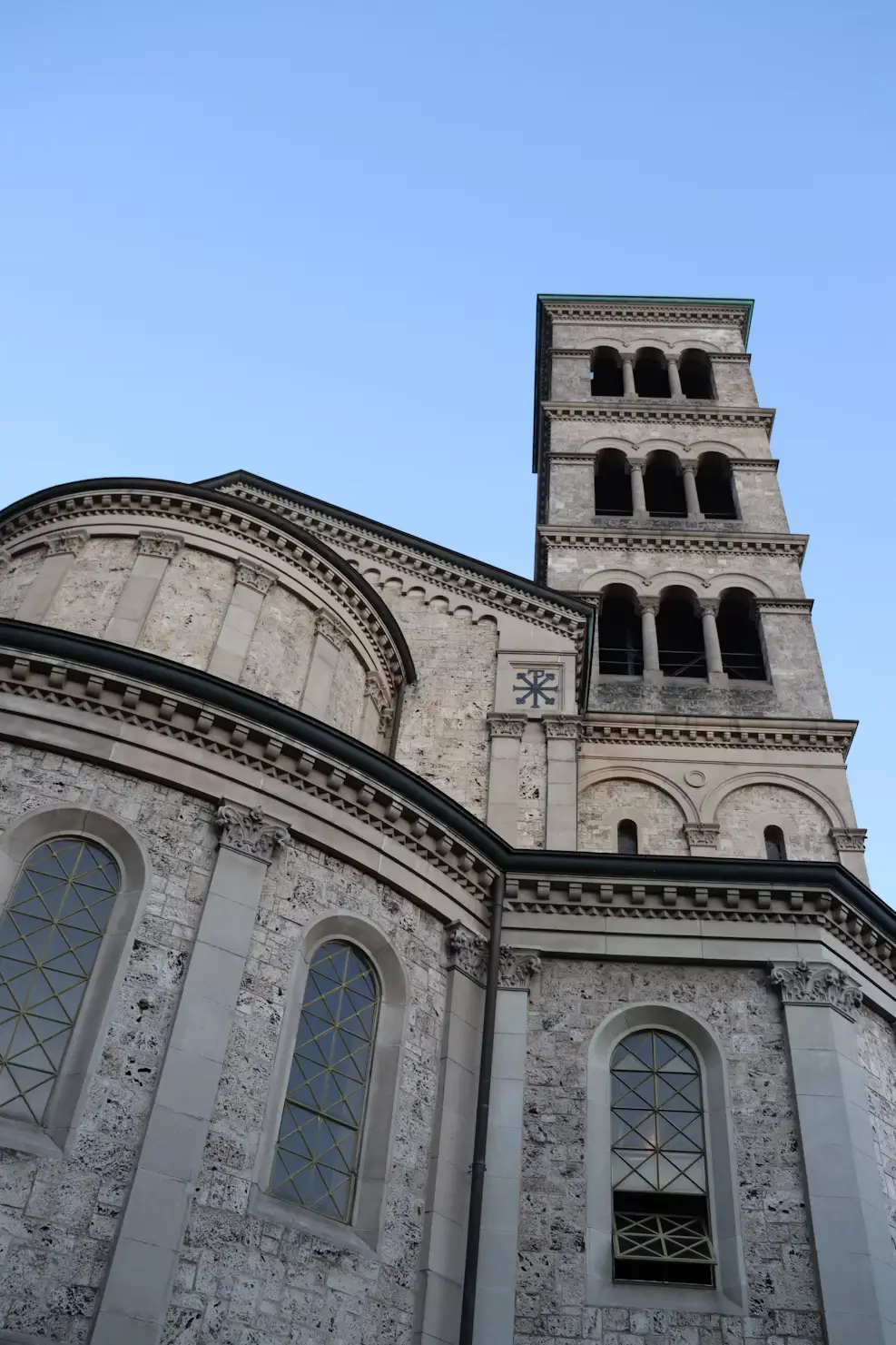 Close-up view of a stone cathedral's tower and rounded apse against a clear blue sky.
